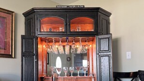 A bar area with a wooden cabinet, wine glasses, and a sign that reads "I'M OUTDOORS...I drink Wine on the Patio".