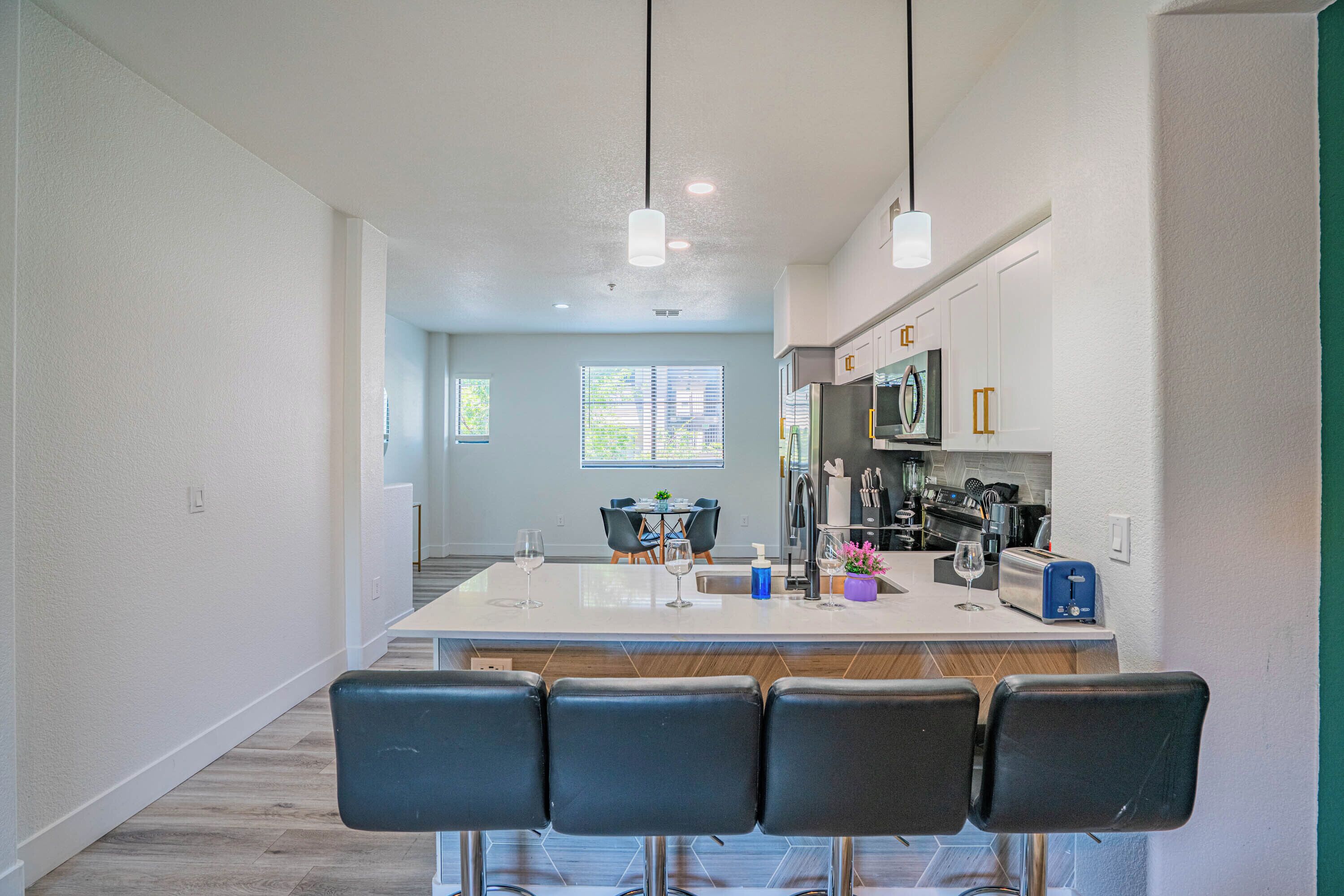 A modern kitchen with a central island, bar stools, and a dining area with a table and chairs.