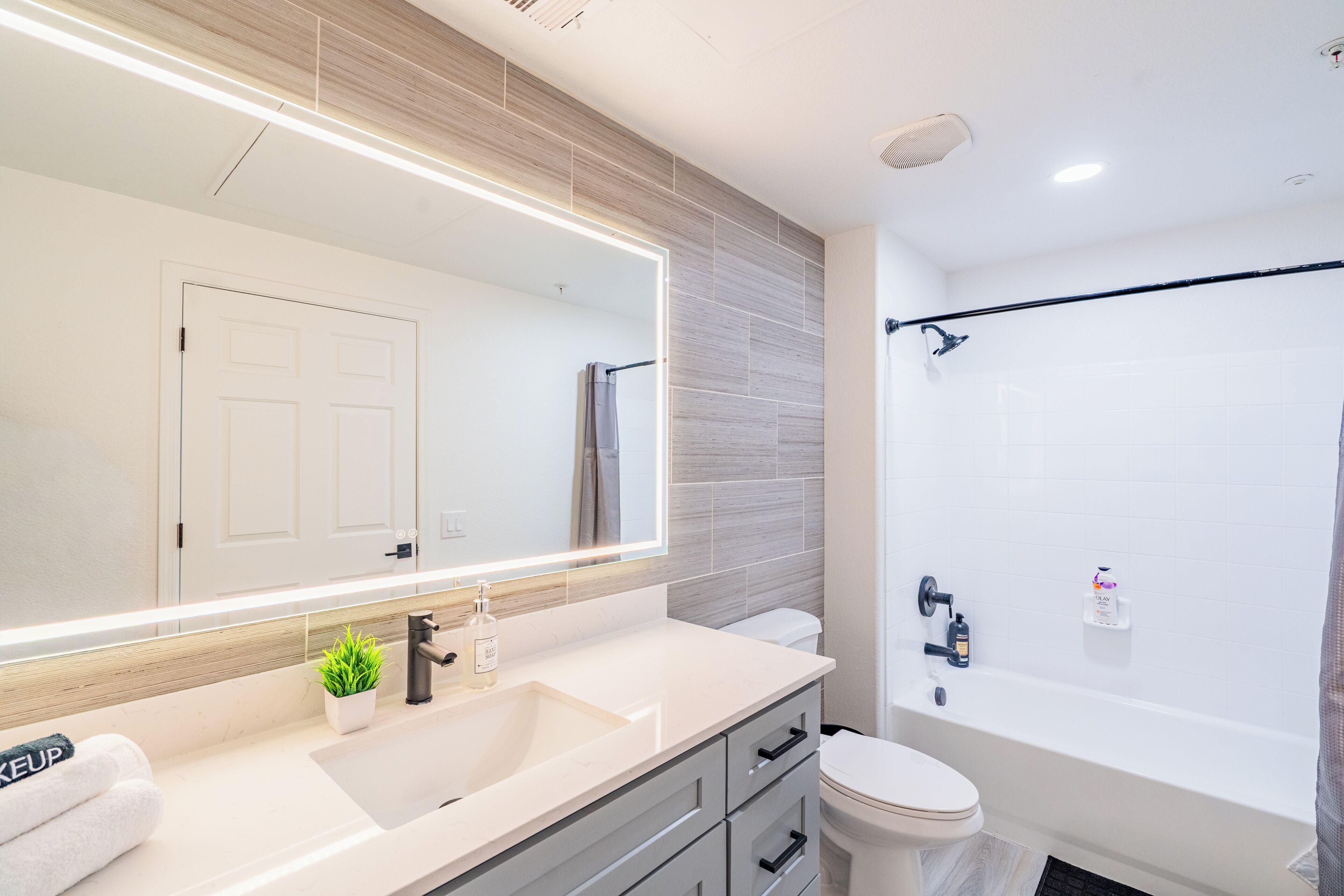 A modern bathroom with a large mirror, a sink, a toilet, and a bathtub.