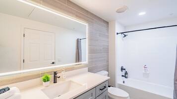 A modern bathroom with a large mirror, a sink, a toilet, and a bathtub.