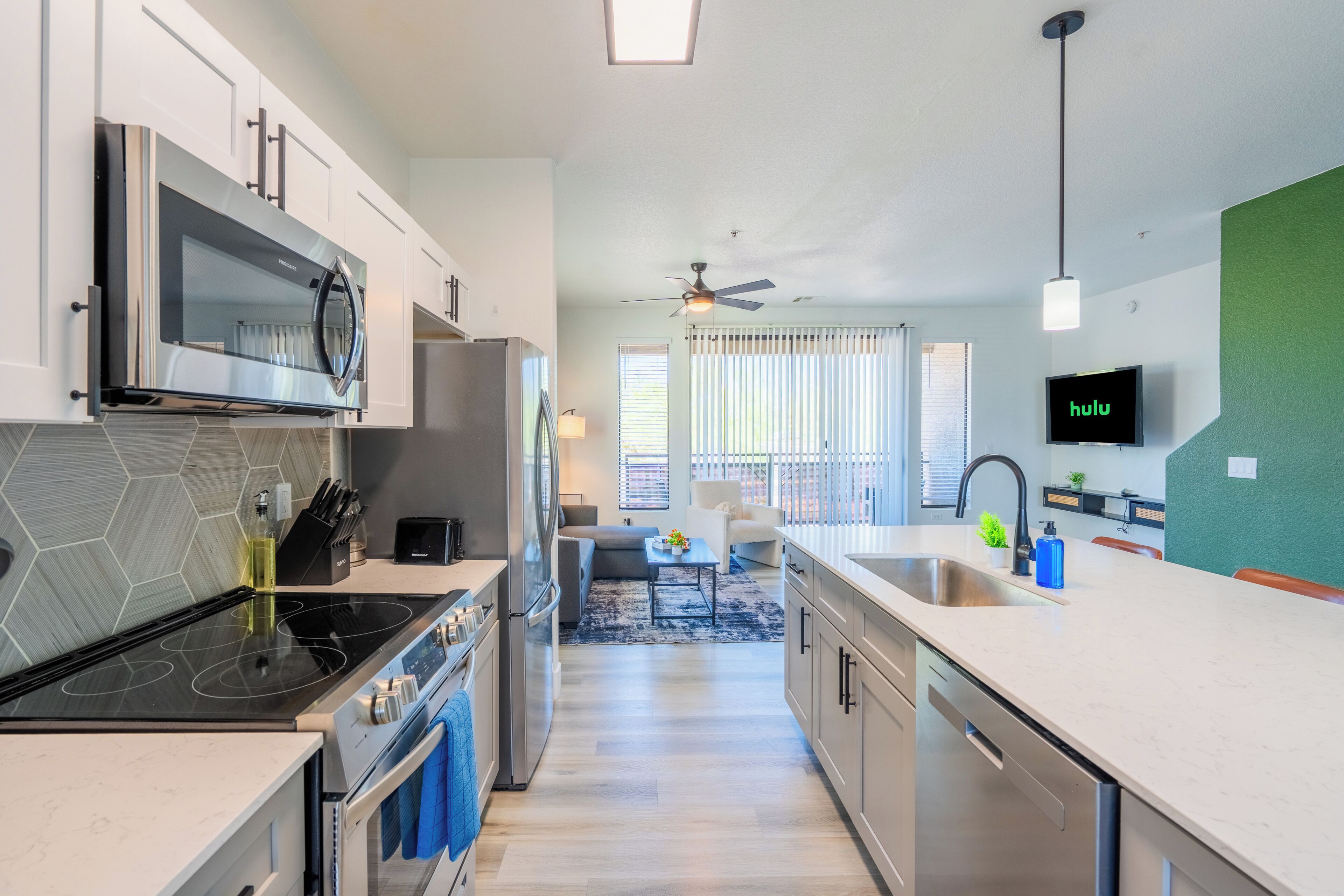 A modern kitchen with a built-in microwave, stove, and dishwasher, a dining area with a table and chairs, and a TV mounted on the wall.