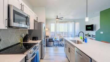 A modern kitchen with a built-in microwave, stove, and dishwasher, a dining area with a table and chairs, and a TV mounted on the wall.