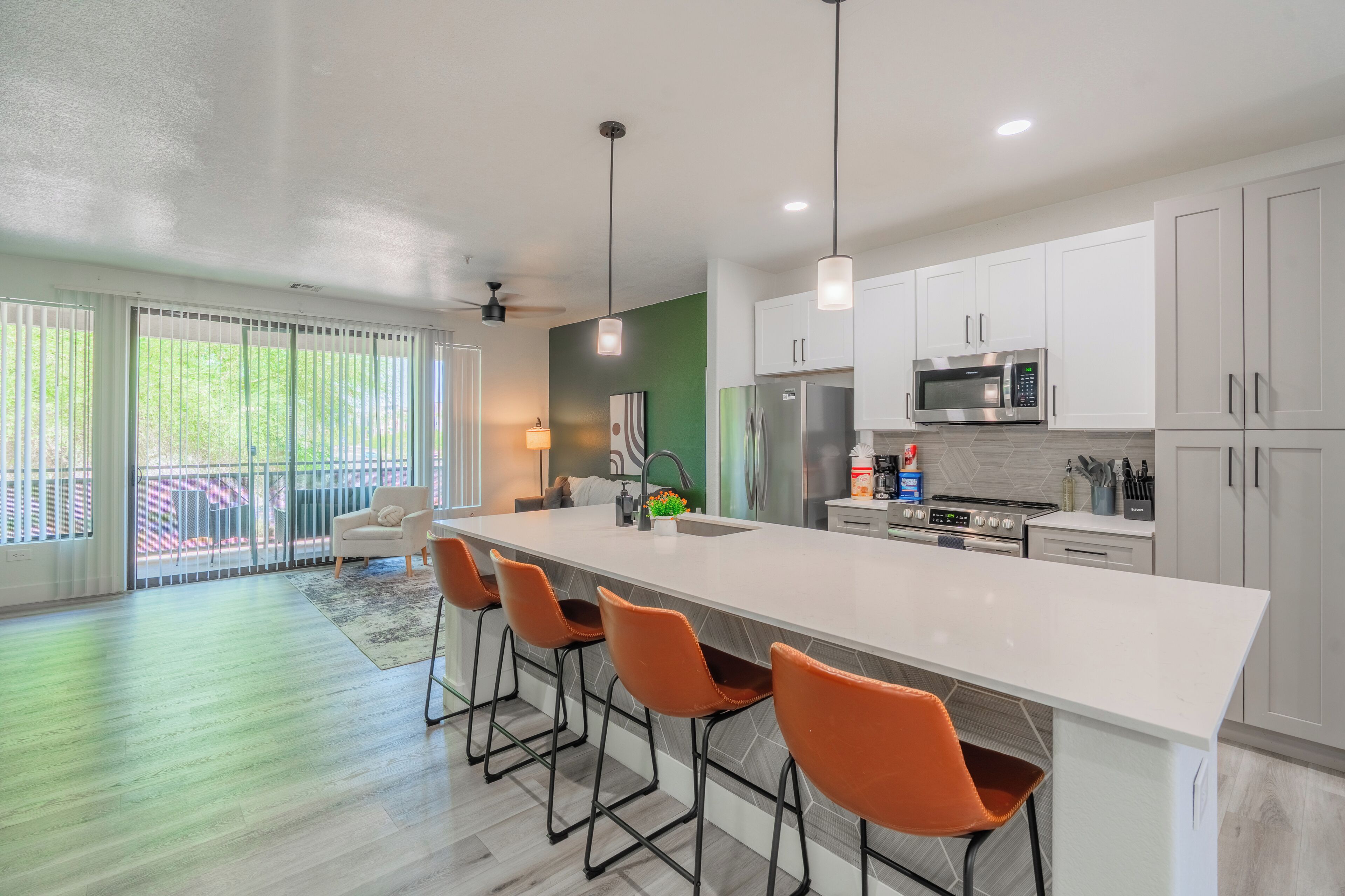 A modern kitchen with a large island, bar stools, white cabinets, and a view to the outside.