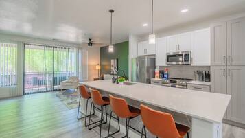 A modern kitchen with a large island, bar stools, white cabinets, and a view to the outside.