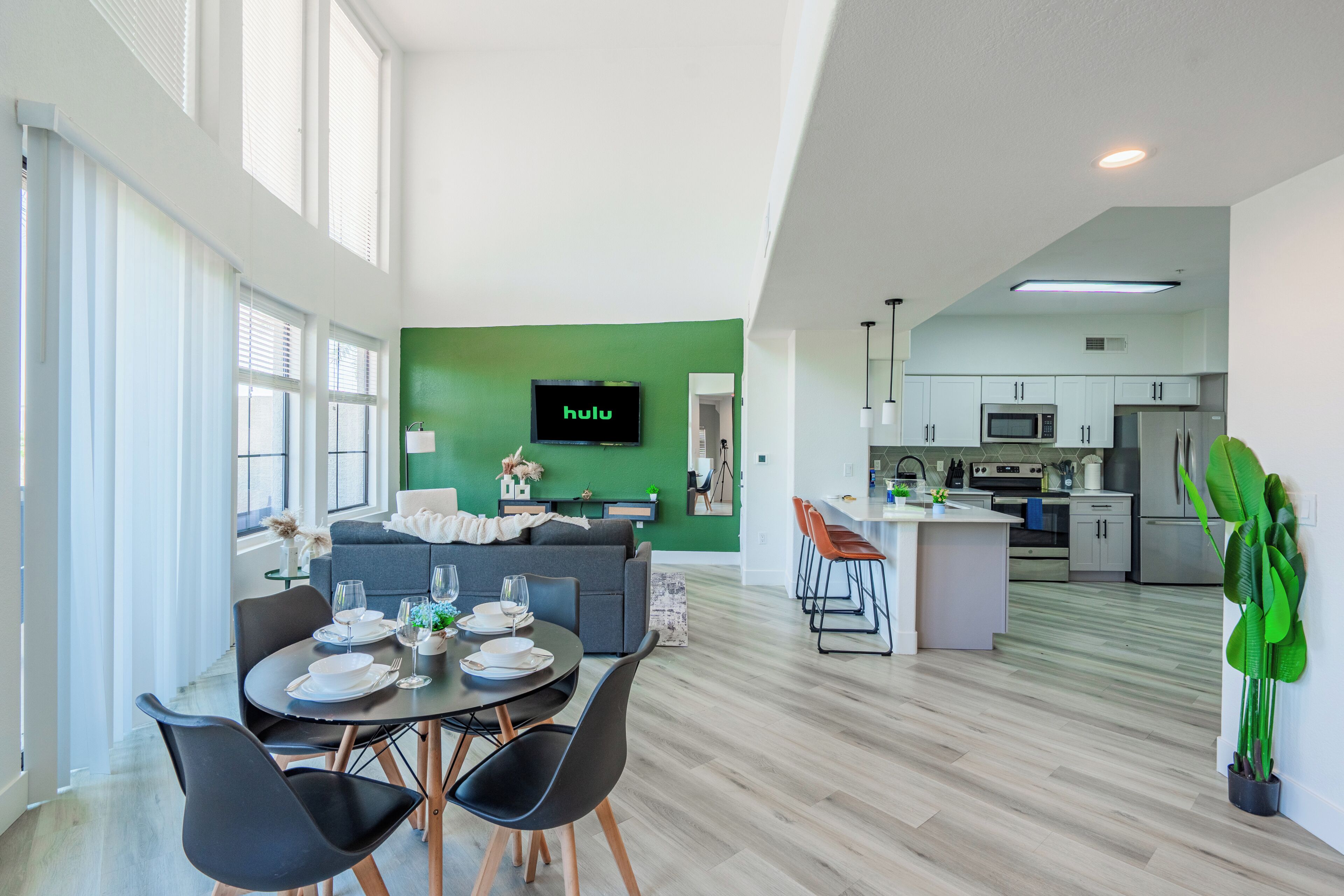 A modern living space with a dining area, kitchen, and a green accent wall.