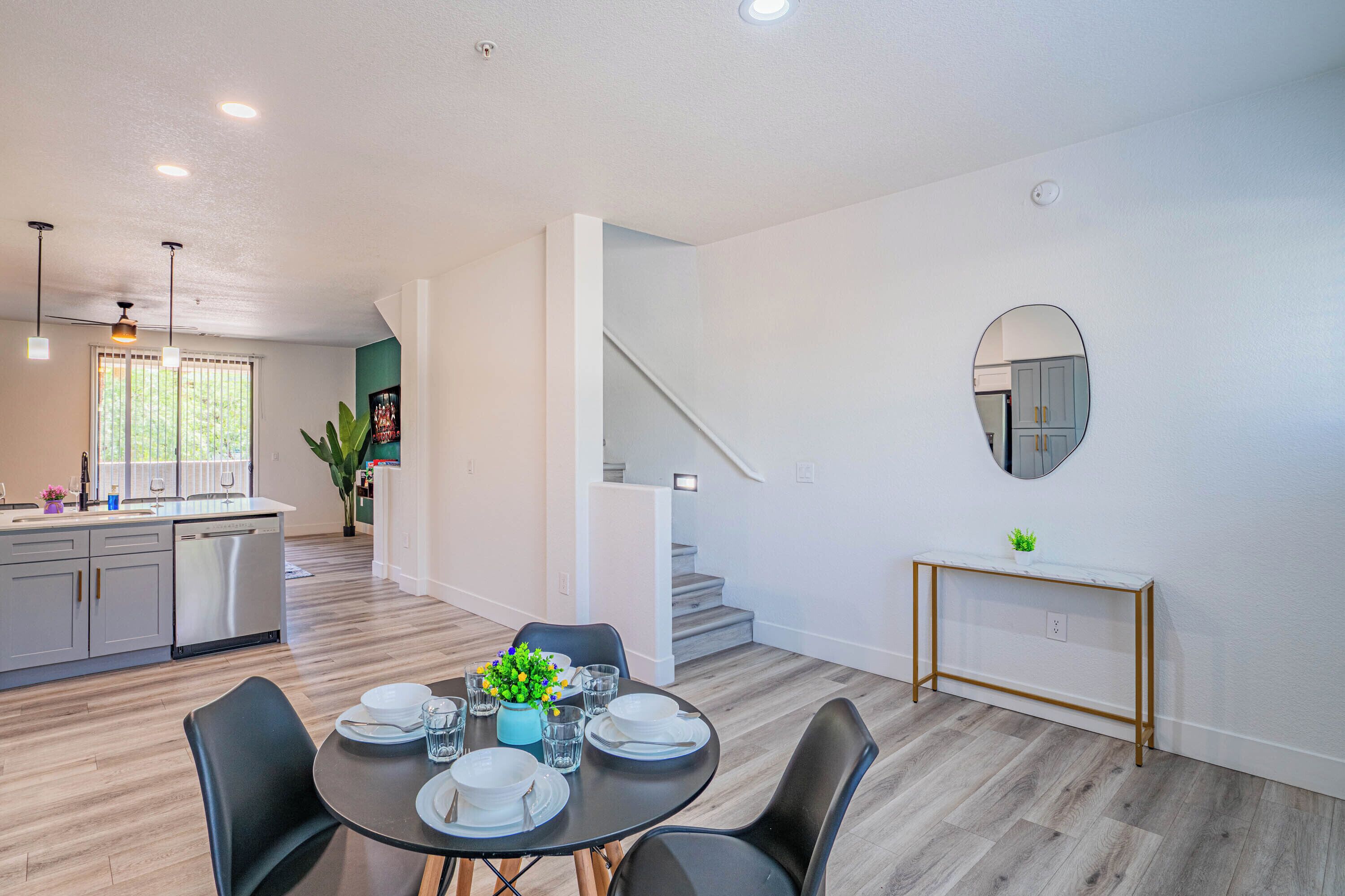 A modern kitchen with a dishwasher, a dining area with a table set for four, and a staircase leading to another level.