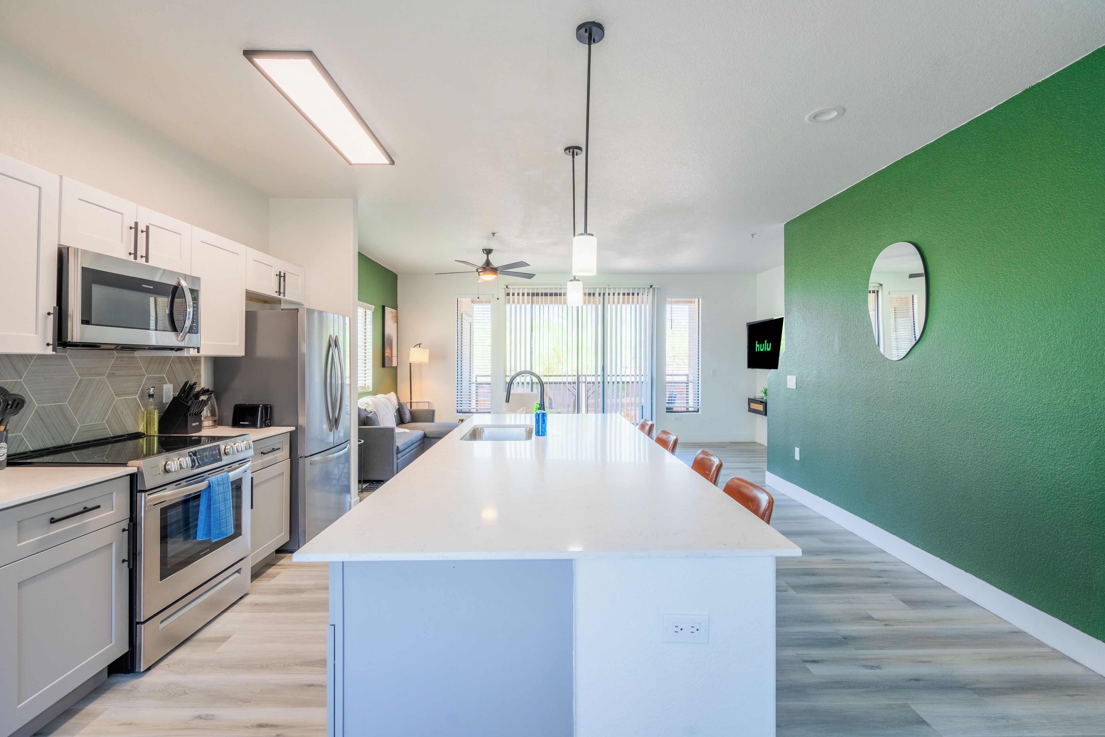 A modern kitchen with white cabinetry, a central island, stainless steel appliances, and a green accent wall.