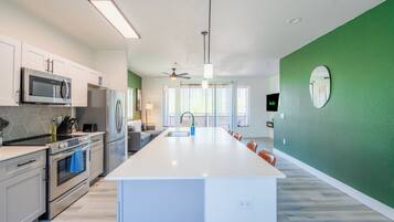 A modern kitchen with white cabinetry, a central island, stainless steel appliances, and a green accent wall.