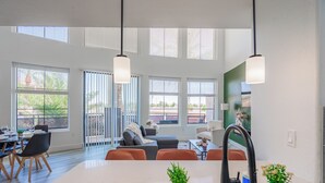 Une cuisine moderne dotée d’un îlot central, d’un coin repas avec des chaises et de grandes fenêtres équipées de stores.