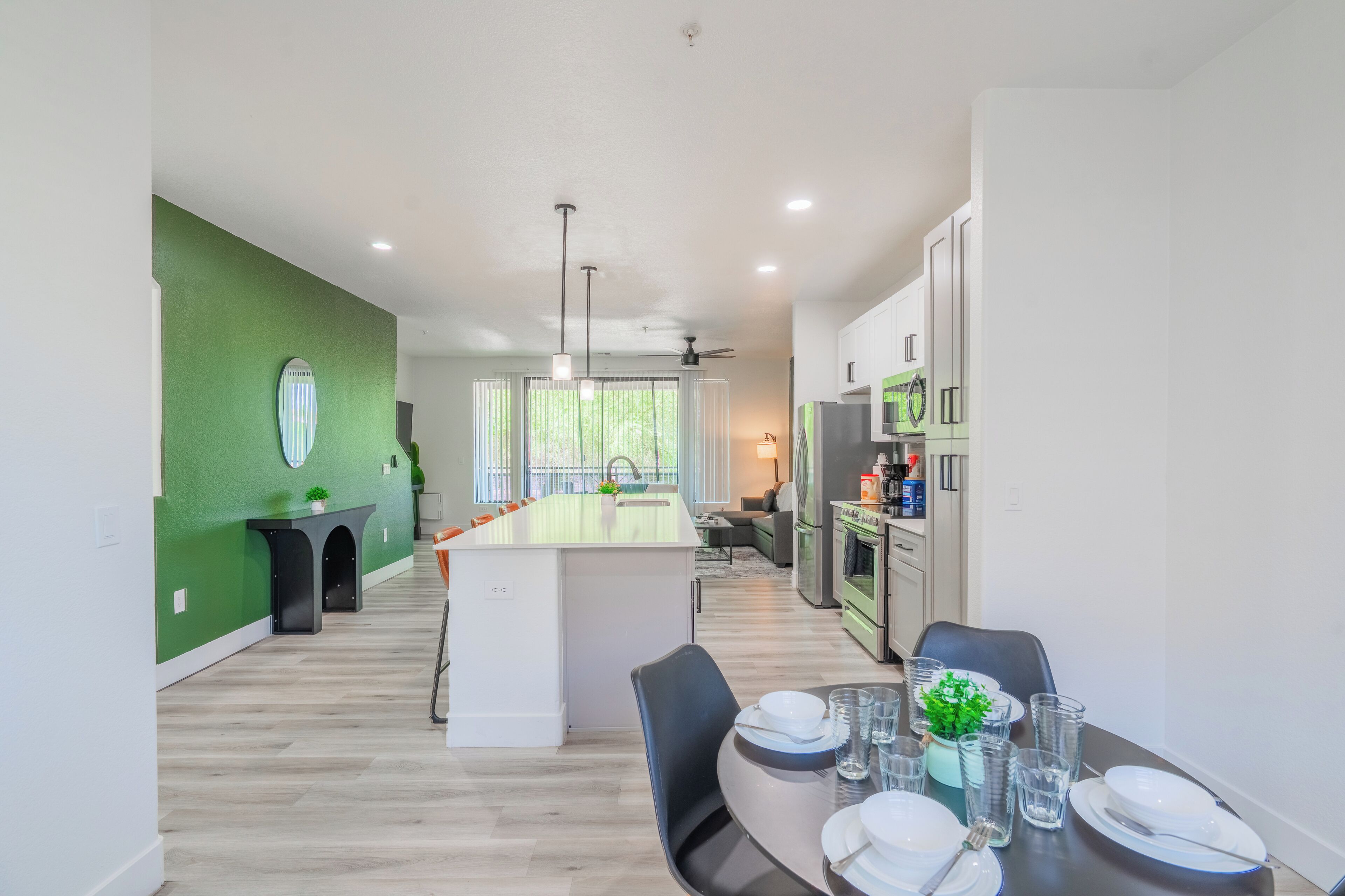 A modern kitchen with a central island, a dining area with a table set for four, and a green accent wall.
