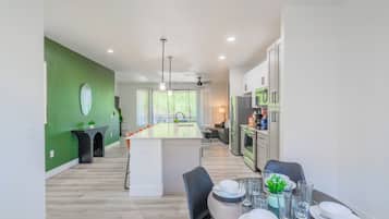 A modern kitchen with a central island, a dining area with a table set for four, and a green accent wall.
