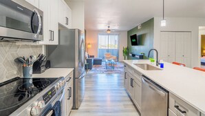 Une cuisine moderne équipée d’appareils électroménagers en acier inoxydable, un coin repas avec un canapé et une table, et une vue sur un salon doté d’un téléviseur.
