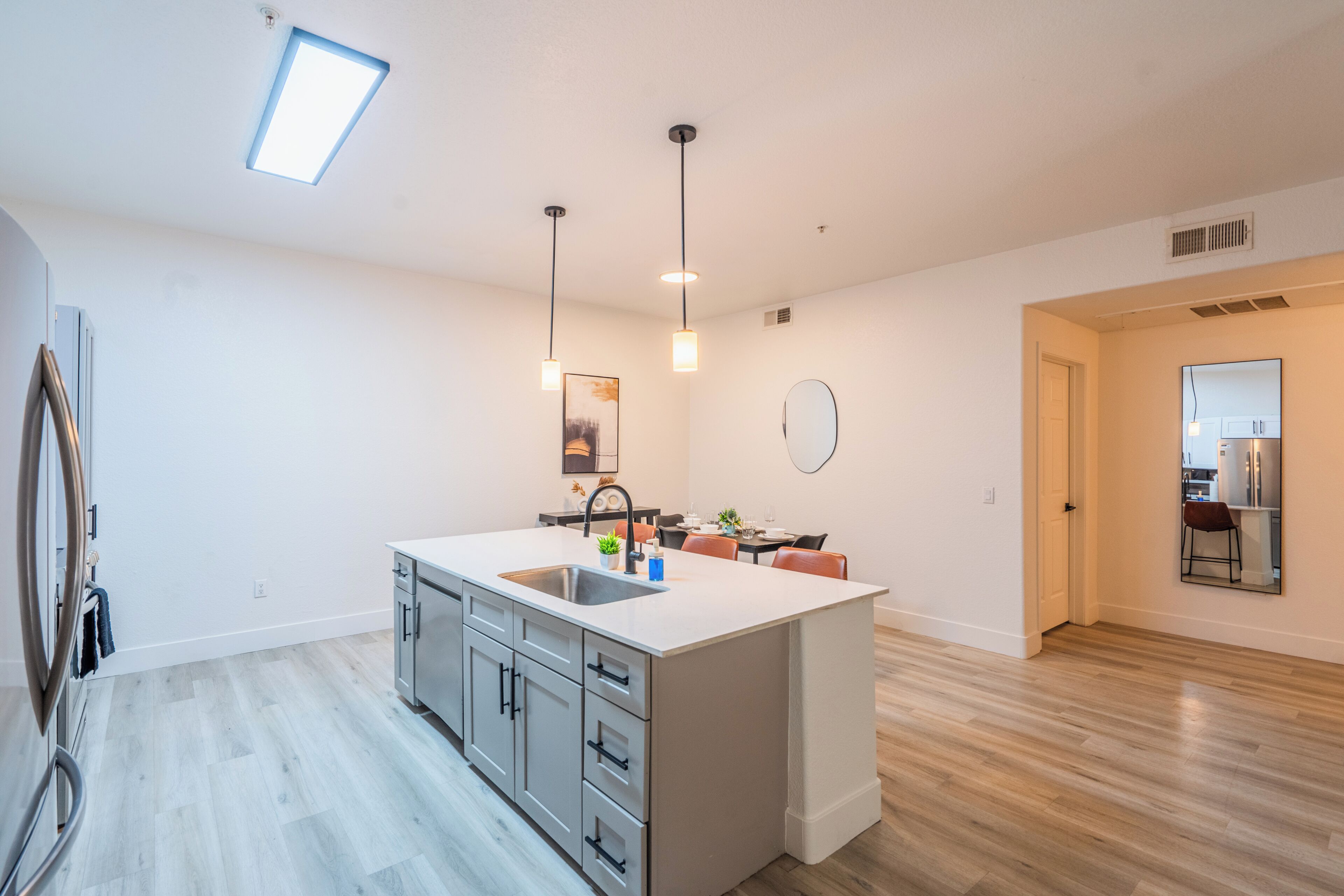 A modern kitchen with a central island, pendant lighting, and a dining area with chairs and a table.