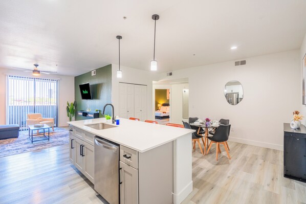 A modern kitchen with a central island, a dining area with a table and chairs, and a living space with a sofa and a coffee table.