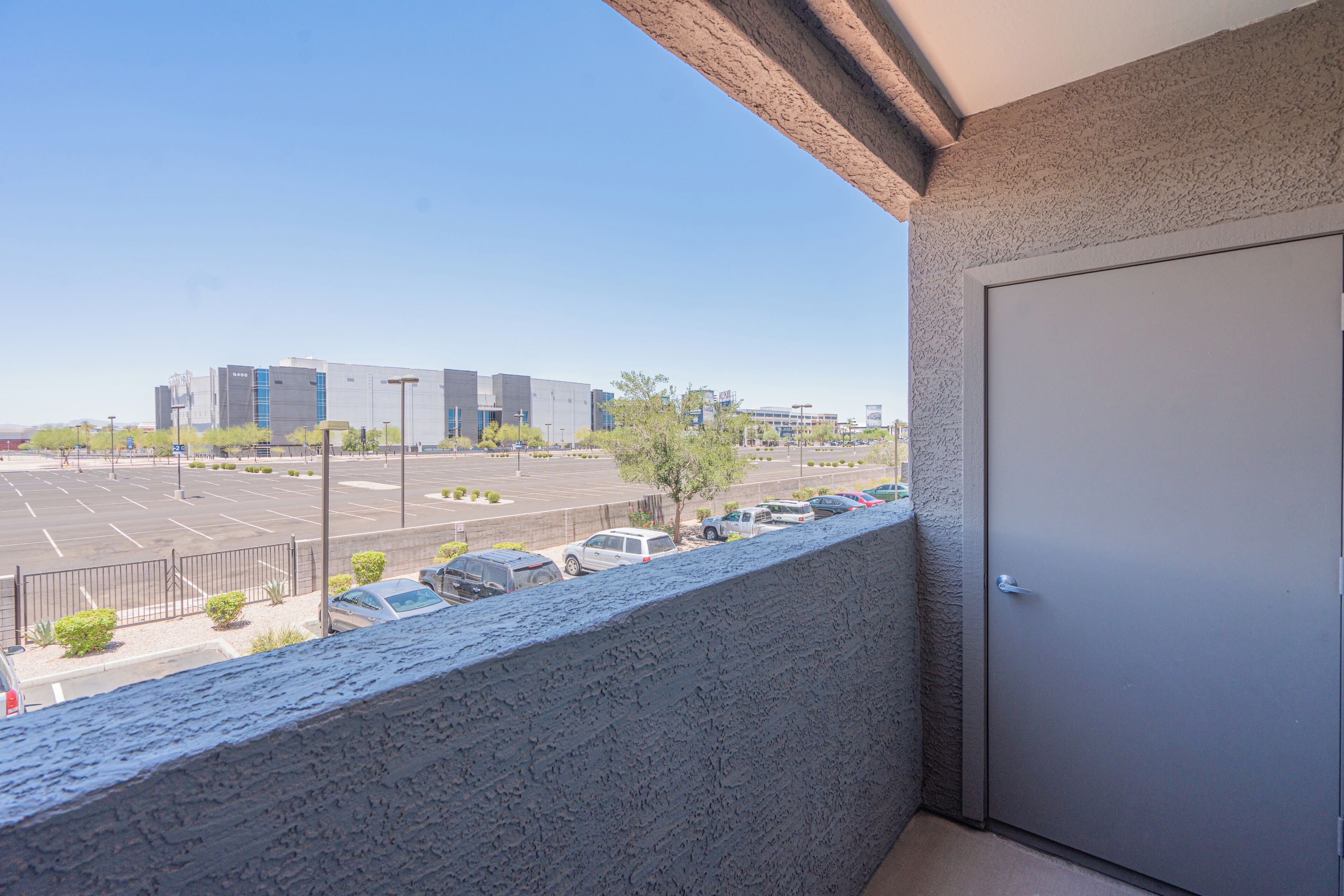 Un balcon donnant sur un parking et sur un bâtiment situé au loin.