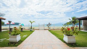 A pathway leading to a beach with potted plants and a view of the ocean. - FLAT NA AREIA DA PRAIA DE GARATUCAIA, ANGRA DOS REIS (Angra dos Reis)