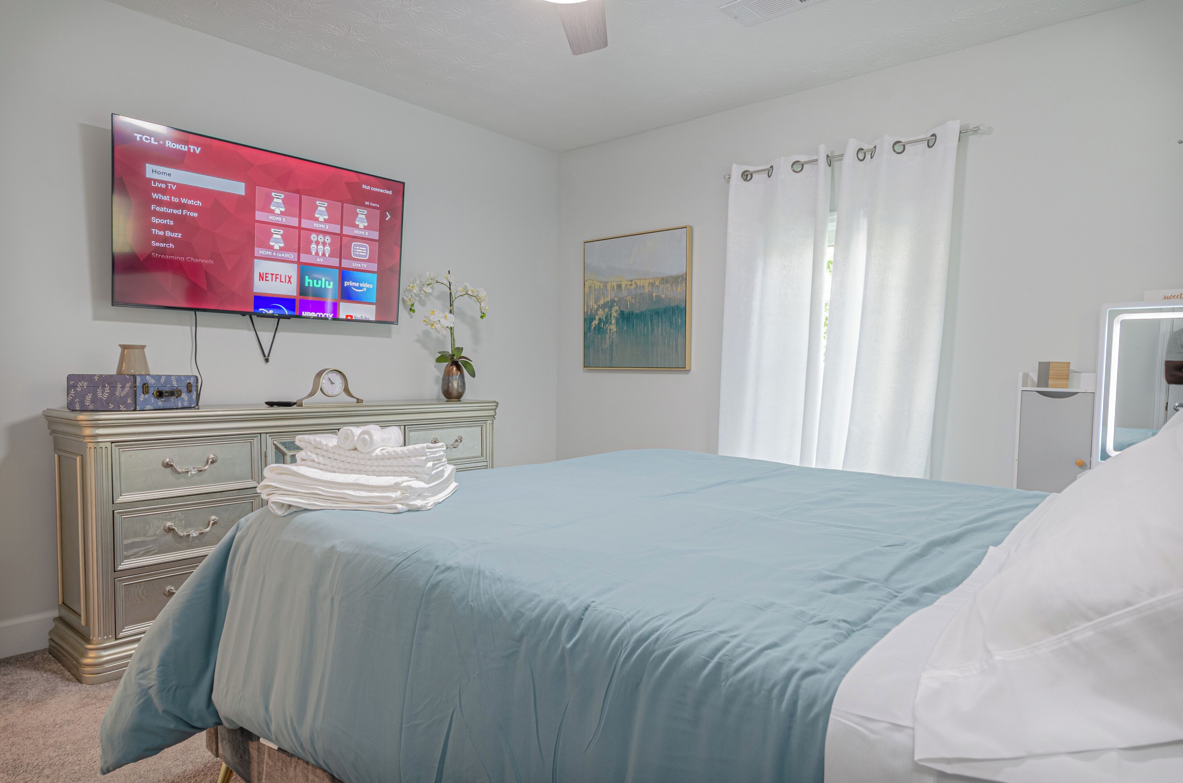 Habitación de hotel con cama, televisión montada en la pared, cómoda, un cuadro y cortina de ducha.