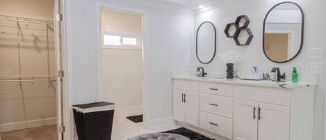 A bathroom with a walk-in shower, a vanity with a mirror, and a black rug.