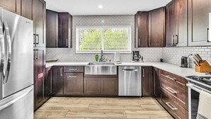 A modern kitchen with dark wood cabinets, stainless steel appliances, and a window with blinds. - Spacious Palm Paradise Retreat -Heated Pool East Delray - Near The Beach- 4/3 (Delray Beach)