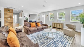 A modern living room with a brown leather sofa, a glass coffee table, and a blue patterned rug. - Spacious Palm Paradise Retreat -Heated Pool East Delray - Near The Beach- 4/3 (Delray Beach)