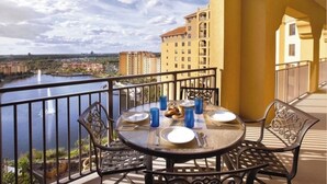A balcony with a table set for two, overlooking a body of water and buildings. - Christmas at Disney! Spacious 2BR Condo w/ Lazy Rivers, Pools, & Fireworks View (Lake Buena Vista)