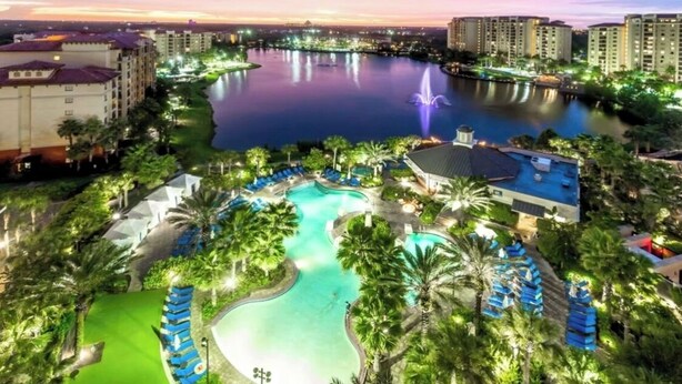 A resort with a large swimming pool, a fountain, and a view of a body of water at dusk. - Christmas at Disney! Spacious 2BR Condo w/ Lazy Rivers, Pools, & Fireworks View (Lake Buena Vista)
