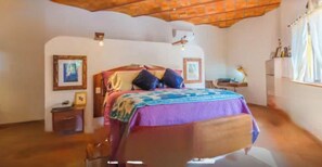 A bedroom with a wooden bed, a nightstand, a desk with a lamp, and a window with curtains.