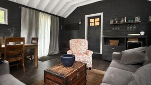 Una sala de estar acogedora con una pared de madera oscura, un sillón estampado, un sofá gris, un aparador de madera y un comedor con sillas y una mesa de madera.