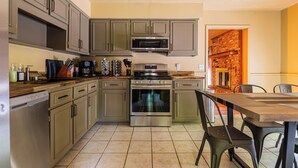 A kitchen with grey cabinets, a stainless steel oven, a microwave, and a brick wall in the background. - Fort Winburn Military Home (Columbus)