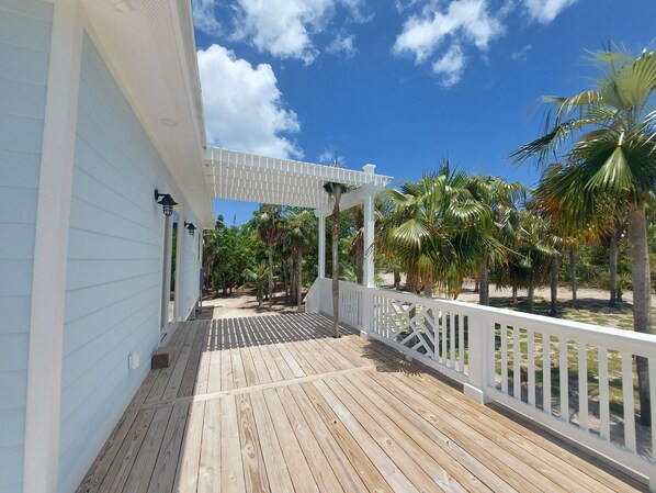 A wooden deck with a white railing, a covered area with a pergola, and palm trees in the background.