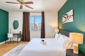 A hotel room with a bed, desk, chair, and a ceiling fan. - Walk To Westgate w/ Modern Pool, Gym, Parking, W/D (Glendale)
