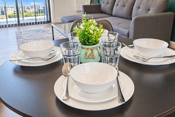 A dining table set with white plates, bowls, glasses, and cutlery, with a green plant centerpiece.