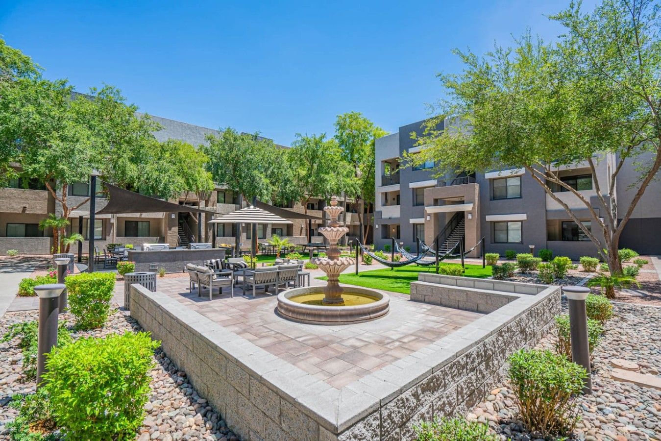 A courtyard with outdoor seating, a central fountain, and a building with multiple balconies.
