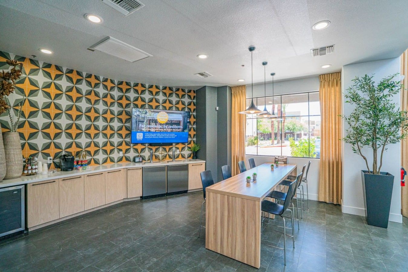 A modern kitchen with a central island, a flat-screen TV mounted on the wall, and a large window providing a view of the outdoors.