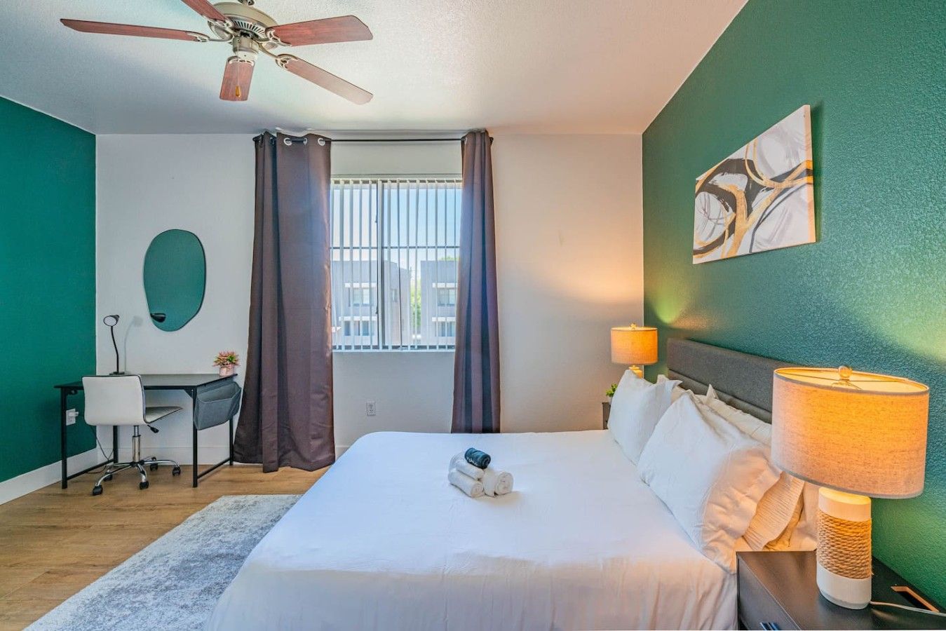 Habitación de hotel con cama, escritorio, silla y ventilador de techo.