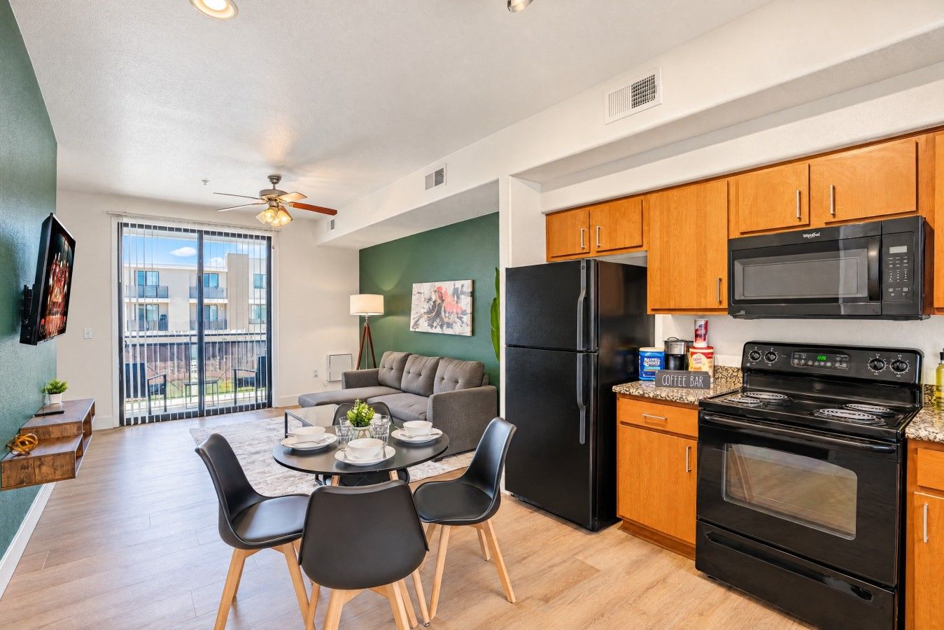 A modern kitchen with a refrigerator, microwave, and stove, a dining area with a table and chairs, and a balcony with a view.