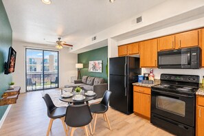 A modern kitchen with a refrigerator, microwave, and stove, a dining area with a table and chairs, and a balcony with a view.