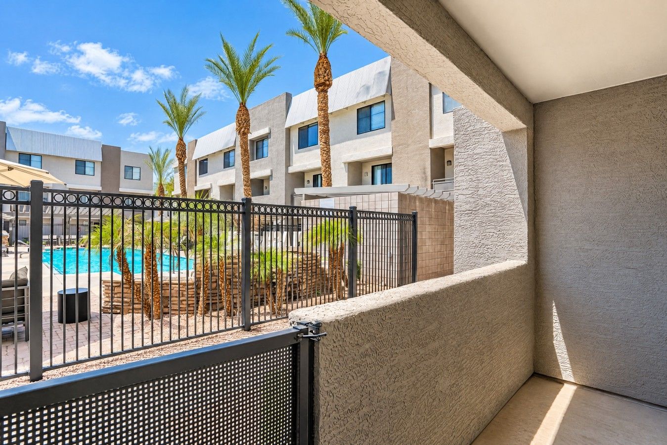 A balcony with a view of a swimming pool, palm trees, and a building with a modern design.