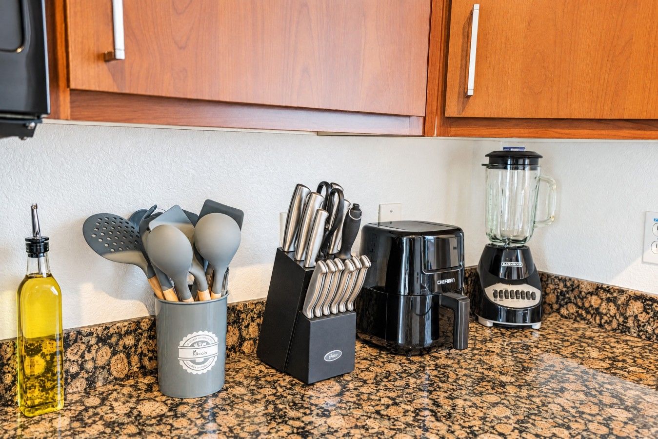A kitchen counter with a coffee maker, a blender, a bottle of olive oil, and a utensil holder.