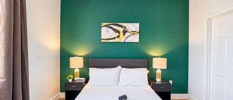 Habitación de hotel con una cama grande, dos mesitas de noche con lámparas, un cuadro en la pared y una puerta blanca.