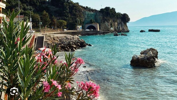 Vista sulla costa con acque blu cristalline, uno scoglio e l'ingresso di una galleria.
