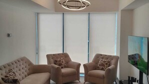 A modern living room with a sectional sofa, two armchairs, a large flat-screen TV, and a unique circular ceiling light.