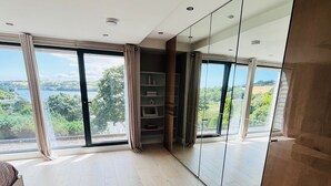 A spacious room with large windows, a built-in wardrobe, and a view of the outdoors. - Spacious Modern Creek View House (Truro)