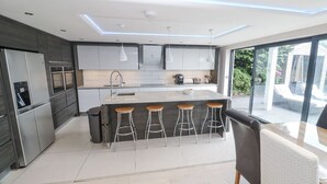 A modern kitchen with a central island, bar stools, and a large window offering a view of the outdoors. - Spacious Modern Creek View House (Truro)