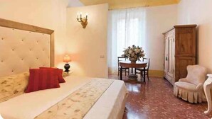 Une chambre à coucher comprenant un lit, une table de chevet, une lampe, une armoire en bois, une table à manger avec des chaises et un arrangement floral.