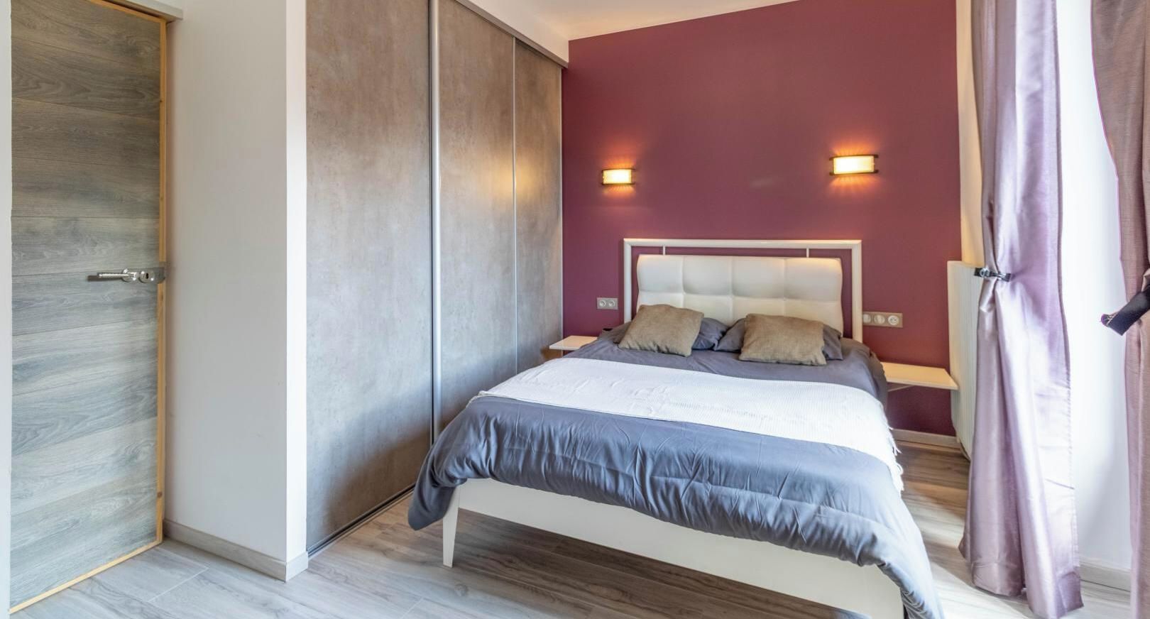 Une chambre à coucher comprenant un lit, une armoire et deux lampes fixées au mur.