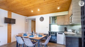 A modern kitchen with stainless steel appliances, a dining area with a wooden table and chairs, and a flat-screen TV mounted on the wall. - LE BÛCHER - VAL CENIS (VAL CENIS)
