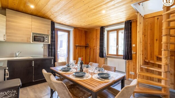 A wooden interior with a dining table set for four, a kitchen with modern appliances, and a wooden staircase. - LE BÛCHER - VAL CENIS (VAL CENIS)