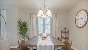 A dining room with a wooden table, leather chairs, a chandelier, a clock, and a window with curtains. - Charming Spacious Home with Game room (Columbus)