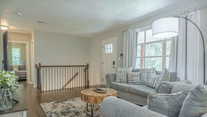 A living room with a grey sofa, a round wooden coffee table, and a large floor lamp. - Charming Spacious Home with Game room (Columbus)
